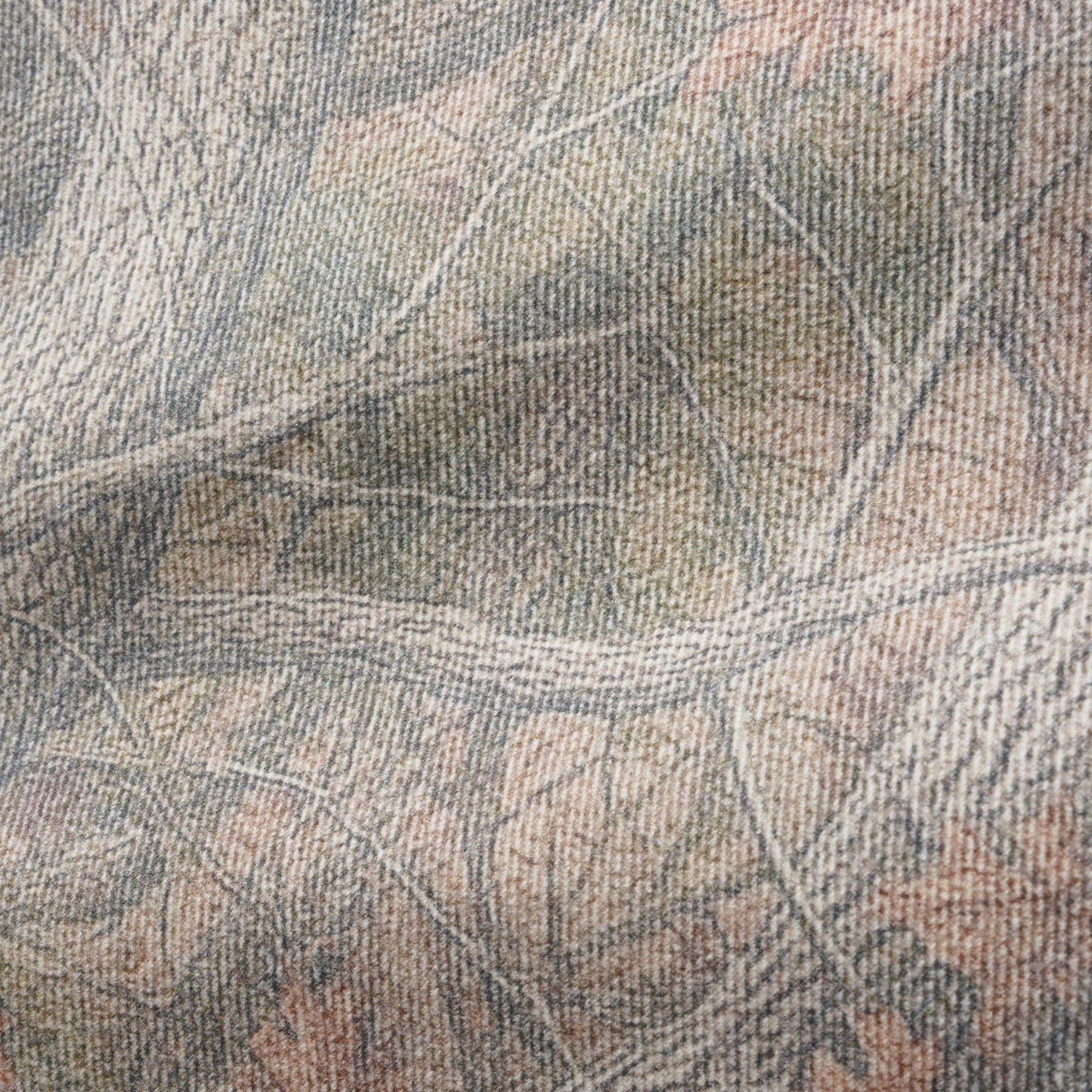A close-up of a woven fabric with a realistic woodland camouflage pattern featuring branches, leaves, and bark in muted shades of gray, beige, brown, and soft orange.