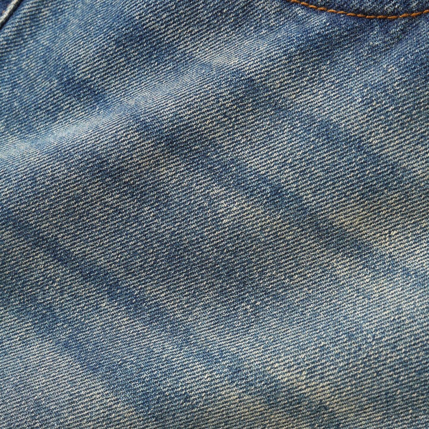 A close-up of blue denim fabric showing the detailed twill weave texture and a subtle light wash.