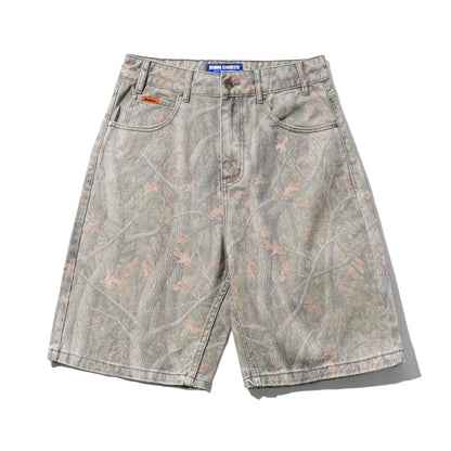 A pair of vintage-style denim shorts featuring a light gray and beige tree-bark camouflage pattern with subtle pinkish leaf details. The shorts have a faded wash, a button fly, belt loops, and a blue waistband label