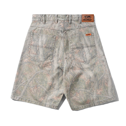 Back view of camouflage denim shorts with a gray, green, and brown woodland branch pattern, featuring a brown leather 'BUTTER' brand patch on the waistband and an orange brand tag on the back pocket.