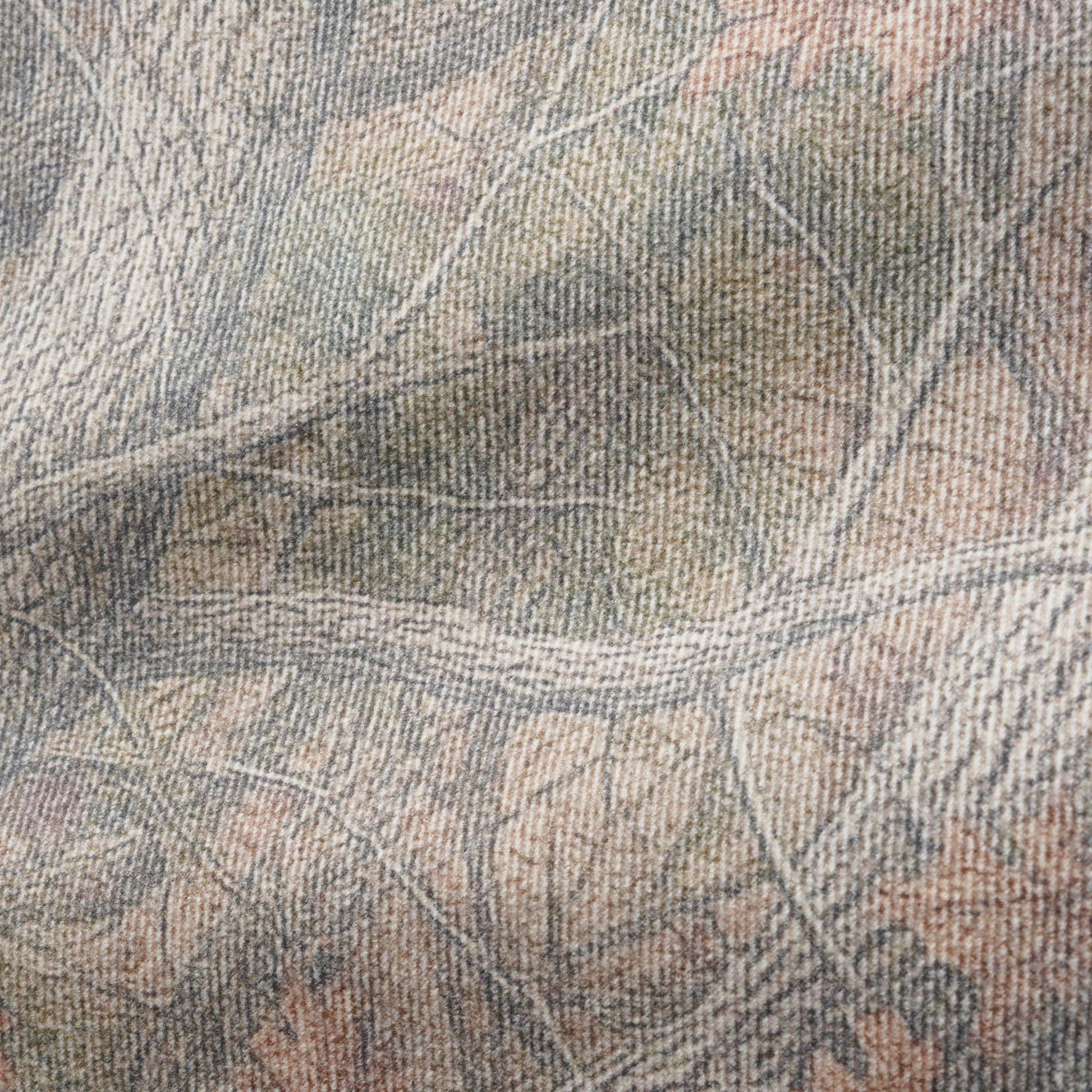 A close-up of a woven fabric with a realistic woodland camouflage pattern featuring branches, leaves, and bark in muted shades of gray, beige, brown, and soft orange.