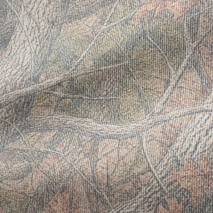 A close-up of a woven fabric with a realistic woodland camouflage pattern featuring branches, leaves, and bark in muted shades of gray, beige, brown, and soft orange.