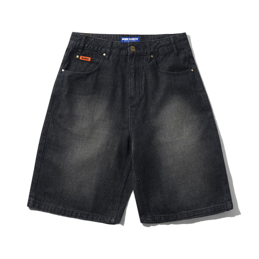 A pair of faded black denim shorts with a subtle wash, featuring classic five-pocket styling, brass-tone rivets, and a small orange brand patch on the front pocket. The brand 'Butter' is visible on the waistband label and the orange patch.