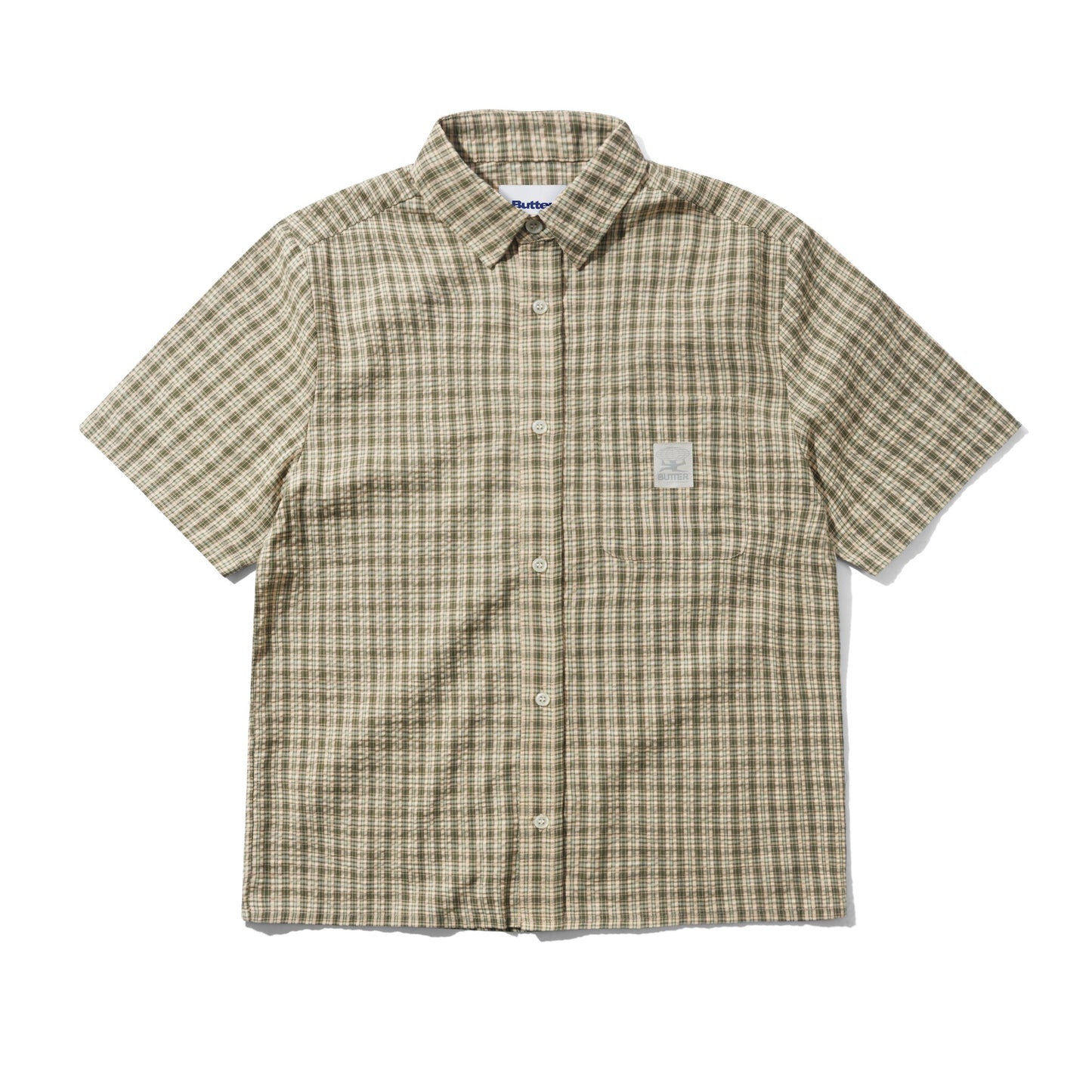 A short-sleeve button-up shirt with a beige and brown plaid pattern, featuring a small white rectangular patch on the left chest, laid flat against a white background.