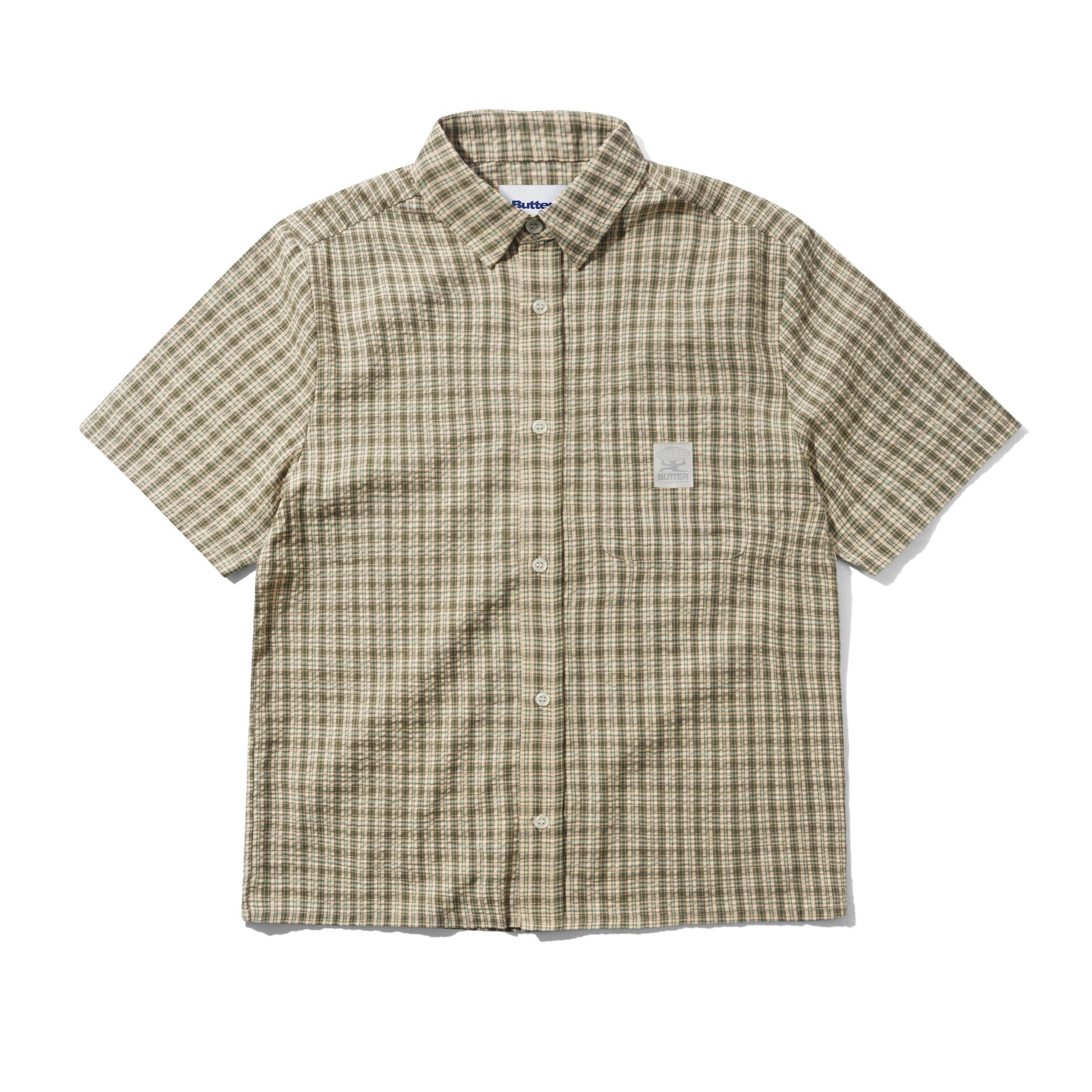A short-sleeve button-up shirt with a beige and brown plaid pattern, featuring a small white rectangular patch on the left chest, laid flat against a white background.