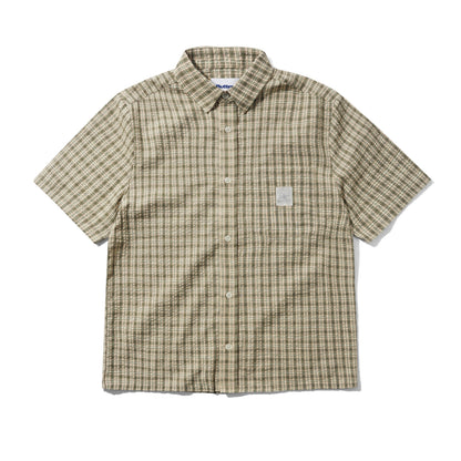 A short-sleeve button-up shirt with a beige and brown plaid pattern, featuring a small white rectangular patch on the left chest, laid flat against a white background.