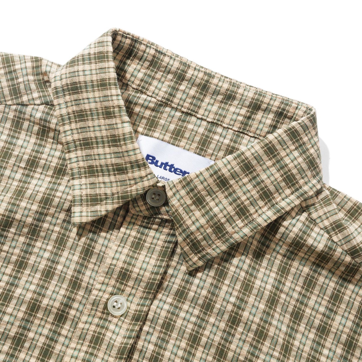 Close-up of a plaid button-down shirt collar with a white Butter brand label visible inside the neck, on a clean white background.