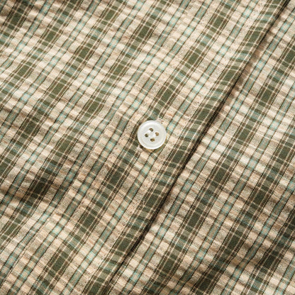 Close-up of a plaid fabric with a white button, showing a pattern of green, beige, and brown intersecting stripes.
