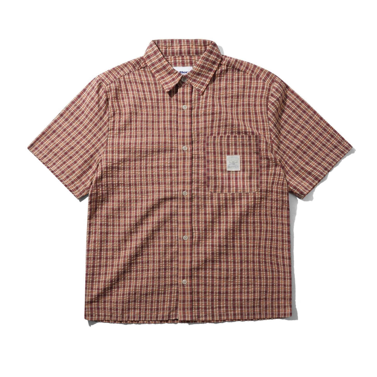 A short-sleeve button-up shirt with a brown, red, and black plaid pattern, featuring a chest pocket with a small woven label, laid flat on a white background.