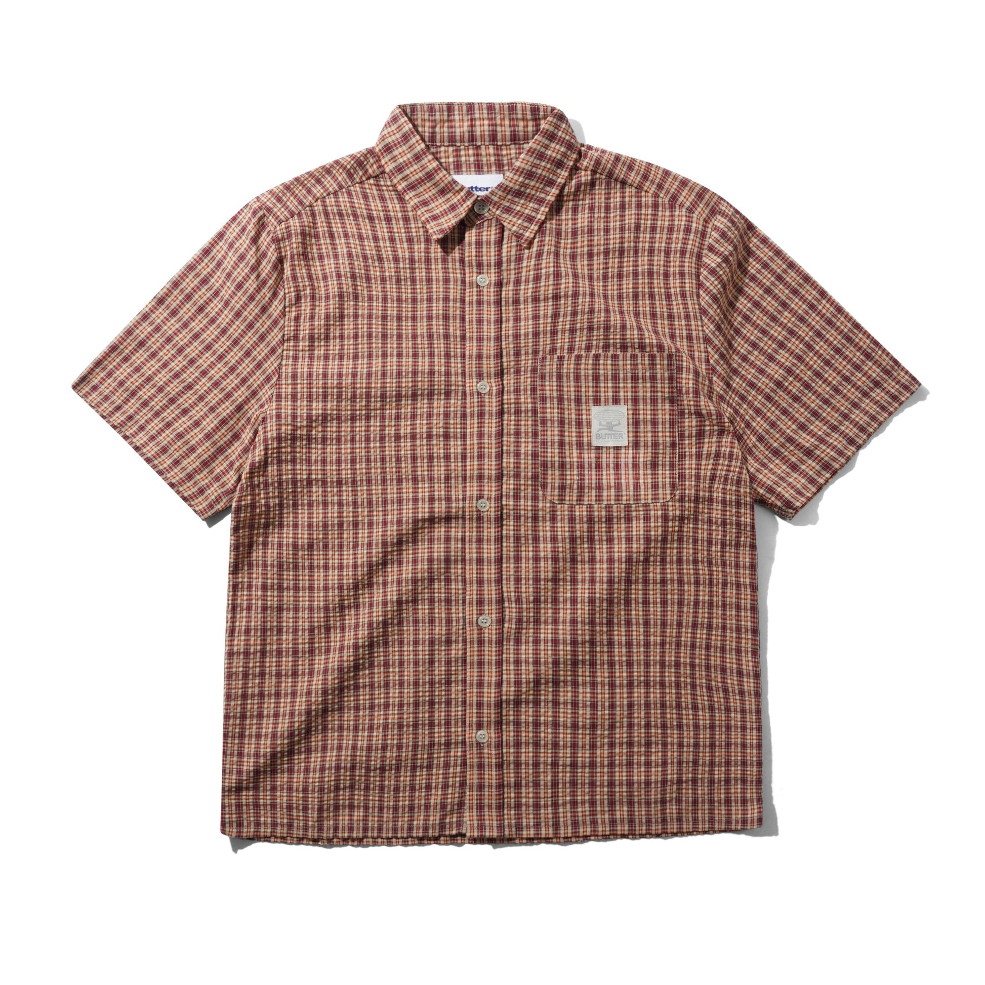 A short-sleeve button-up shirt with a brown, red, and black plaid pattern, featuring a chest pocket with a small woven label, laid flat on a white background.