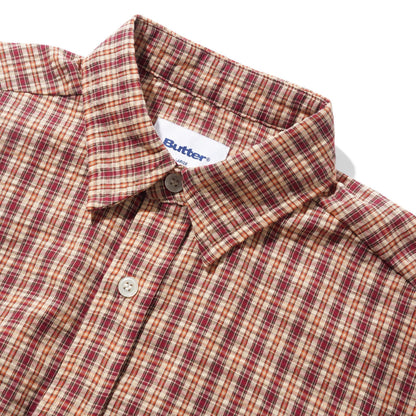 Close-up of a Butter brand plaid button-down shirt in a red, beige, and brown pattern, showing the collar, button, and inner neck label on a white background.