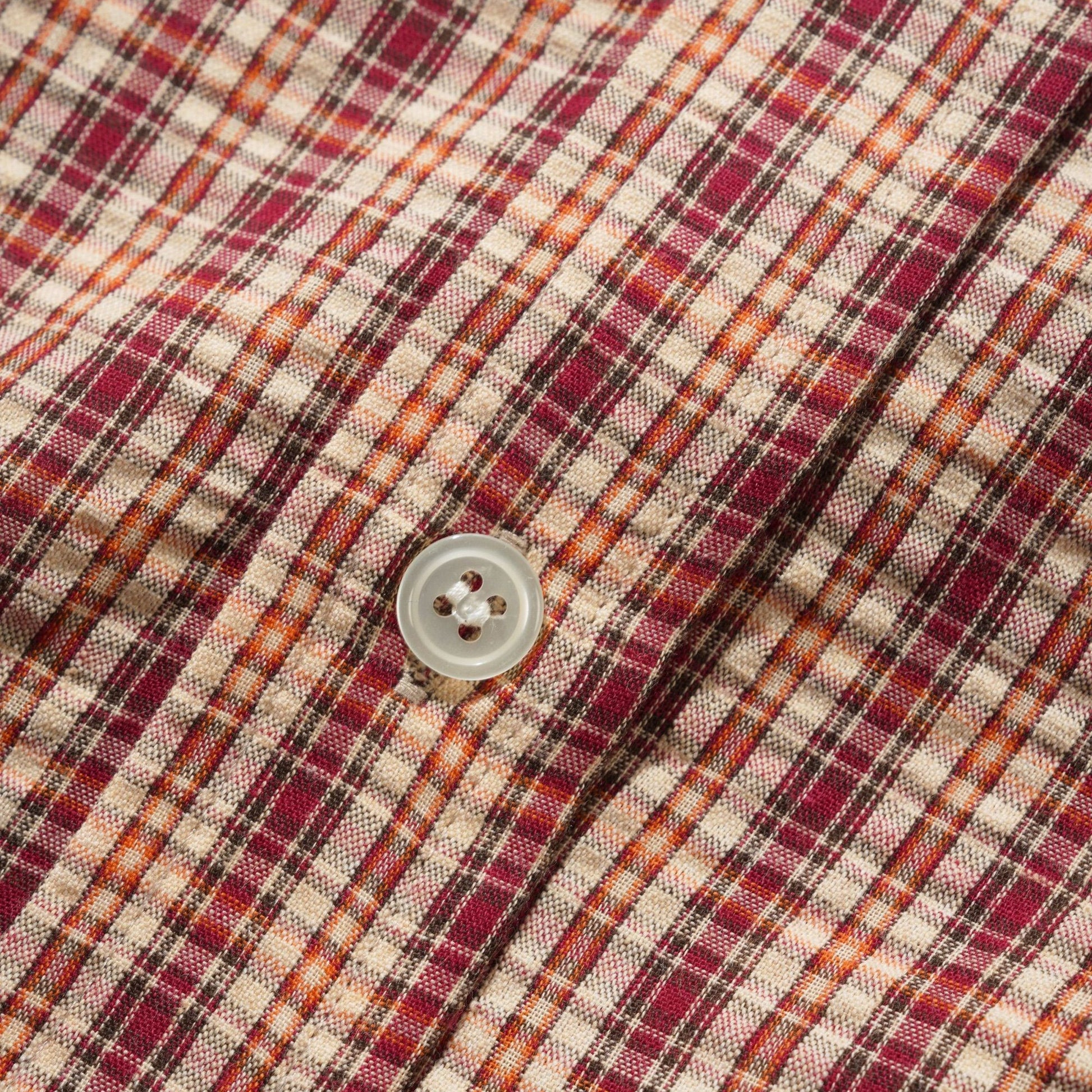 Close-up of a plaid fabric with a single light-colored button, showing a pattern of red, orange, brown, and beige stripes.