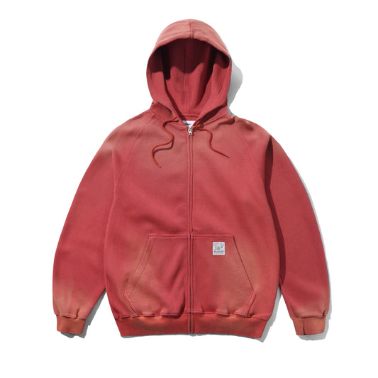 A faded red full-zip hoodie with drawstrings, a front kangaroo pocket, and a small square brand patch on the lower pocket, shown flat against a white background.