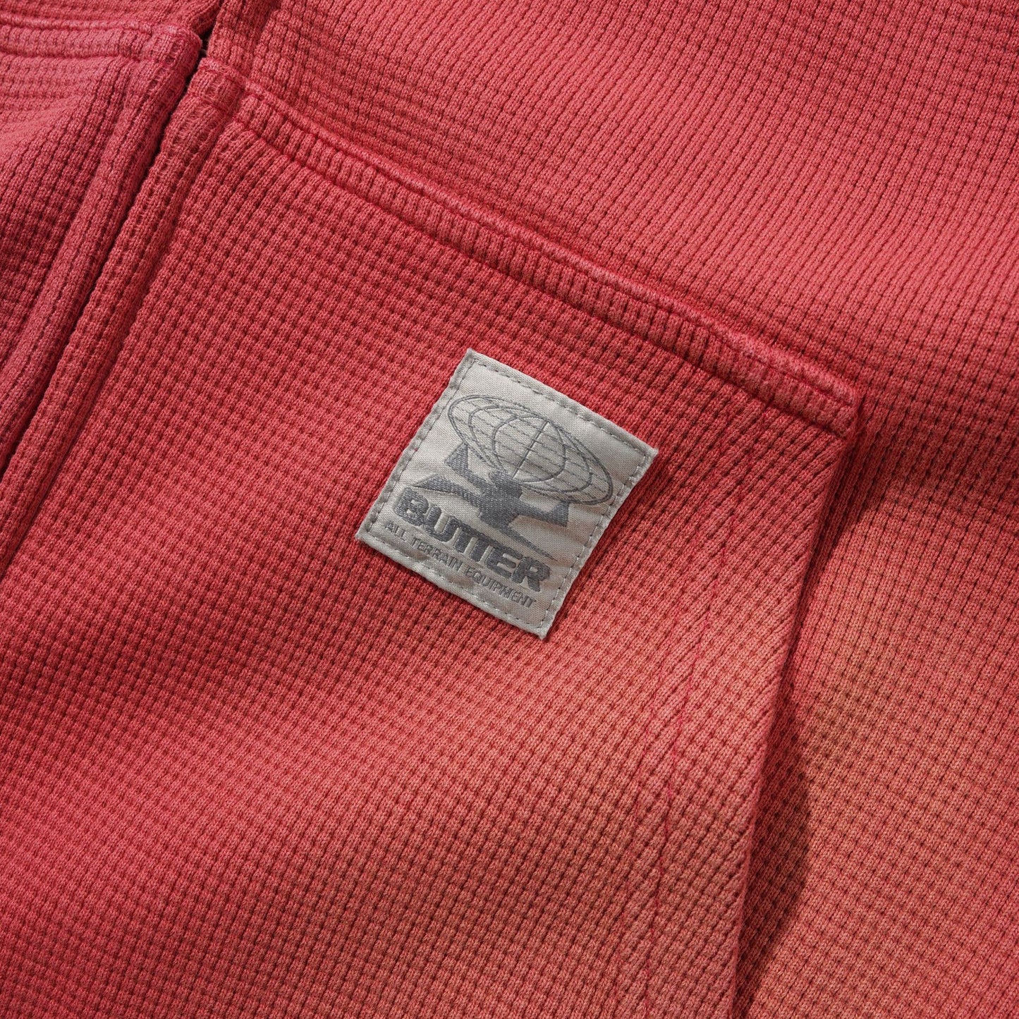 Close-up of a red waffle-knit garment with a sewn-on square brand patch reading OUTER on the chest.