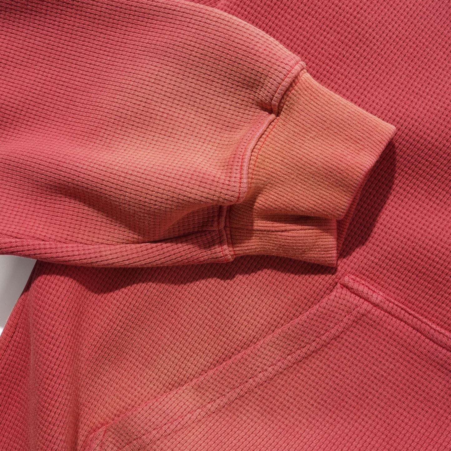 Close-up of a faded red textured knit garment, showing the sleeve cuff and ribbed fabric detail.