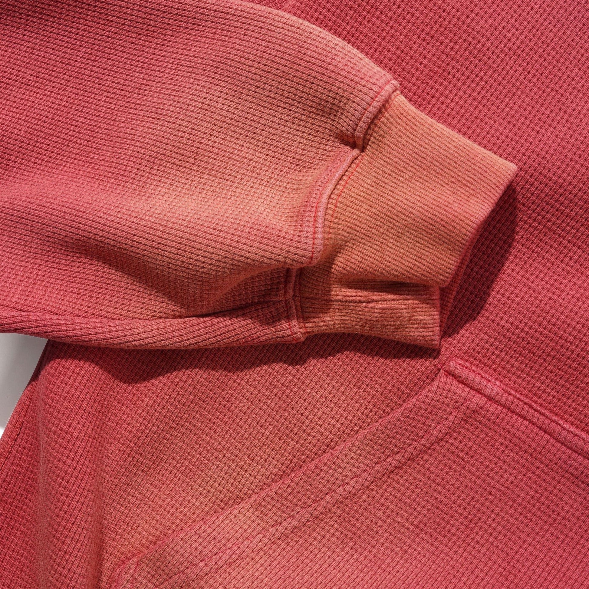 Close-up of a faded red textured knit garment, showing the sleeve cuff and ribbed fabric detail.