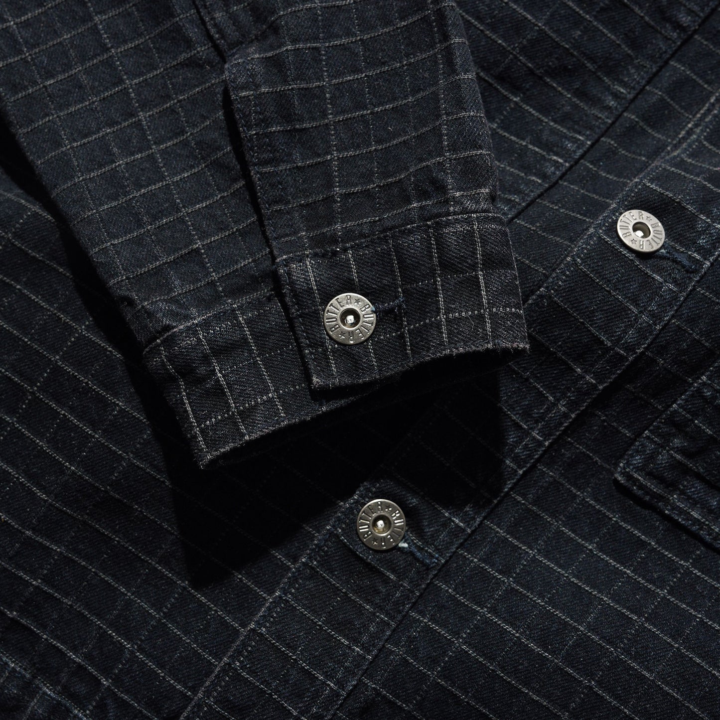 Close-up of a dark charcoal gray plaid overshirt or shirt jacket, showing the fabric texture, button details, and pocket construction.