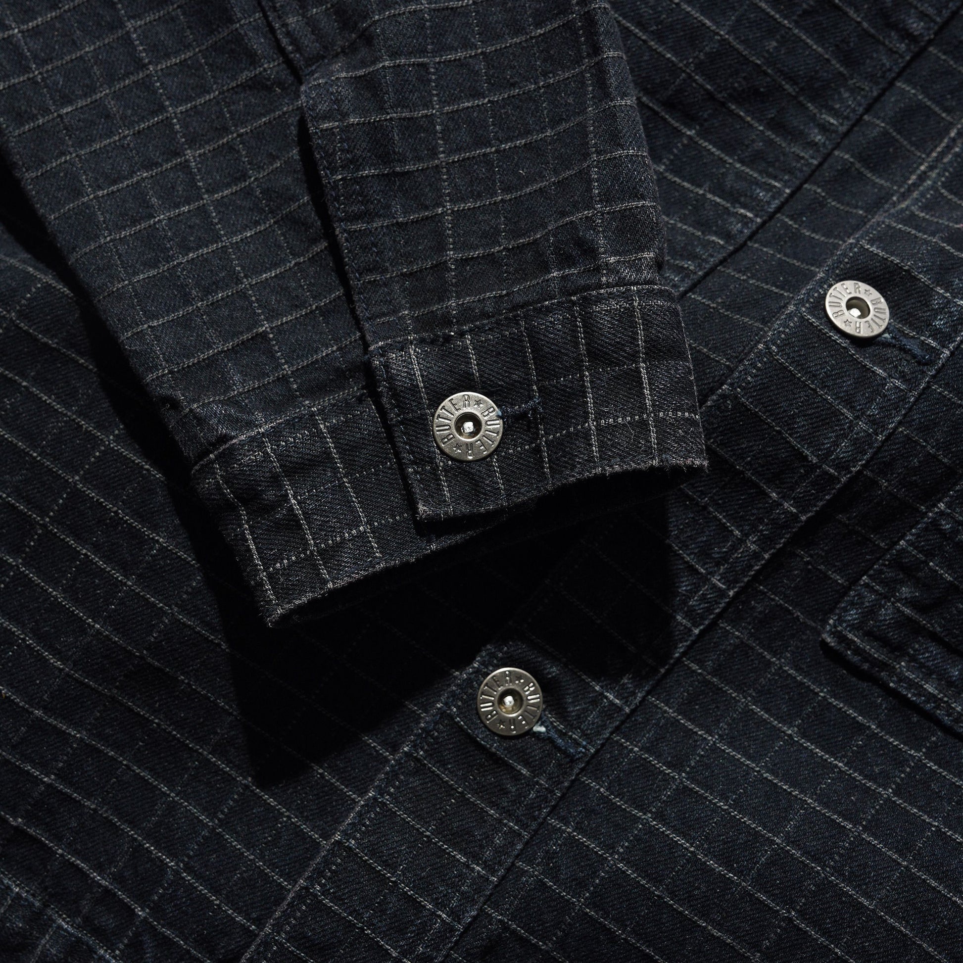 Close-up of a dark charcoal gray plaid overshirt or shirt jacket, showing the fabric texture, button details, and pocket construction.
