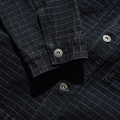 Close-up of a dark charcoal gray plaid overshirt or shirt jacket, showing the fabric texture, button details, and pocket construction.