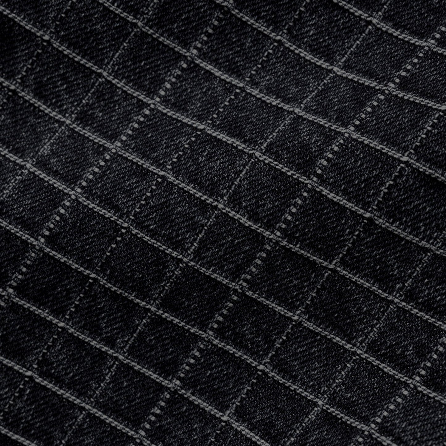 Close-up of a black fabric with a subtle diagonal grid pattern formed by lighter gray stitched lines.
