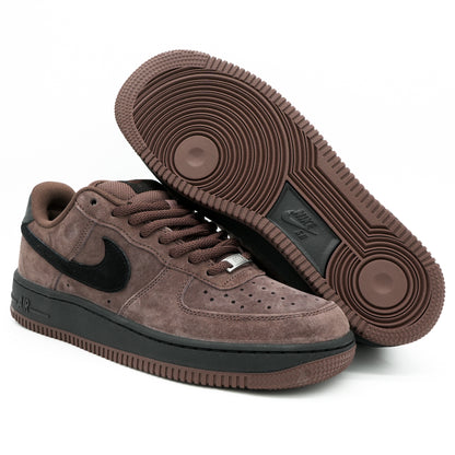A pair of Nike Air Force 1 Low sneakers in a brown suede and black leather combination, with one shoe showing the side profile and the other showing the textured brown outsole.