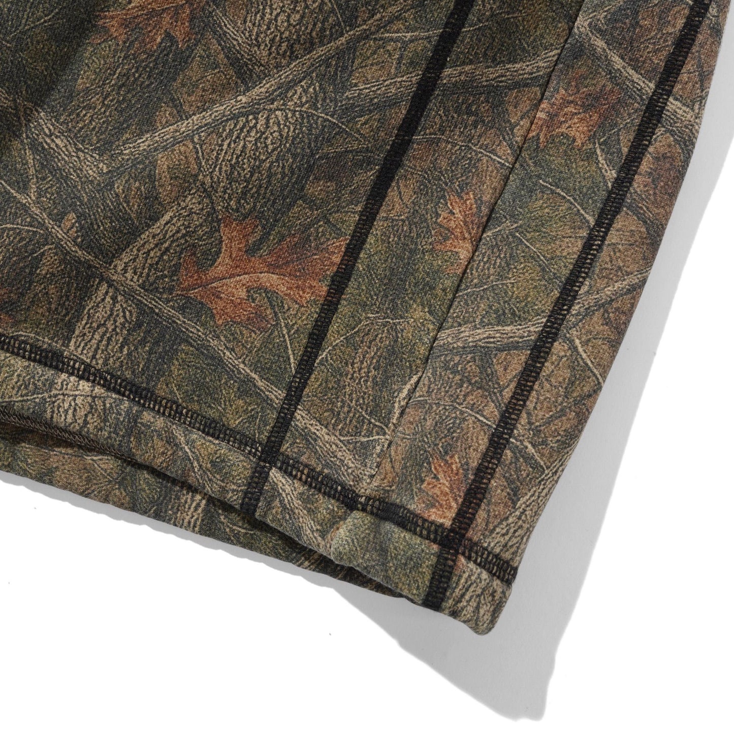 Close-up of a camouflage-patterned fabric with a realistic woodland print in brown, green, and tan, featuring a black stitched border on a white background.