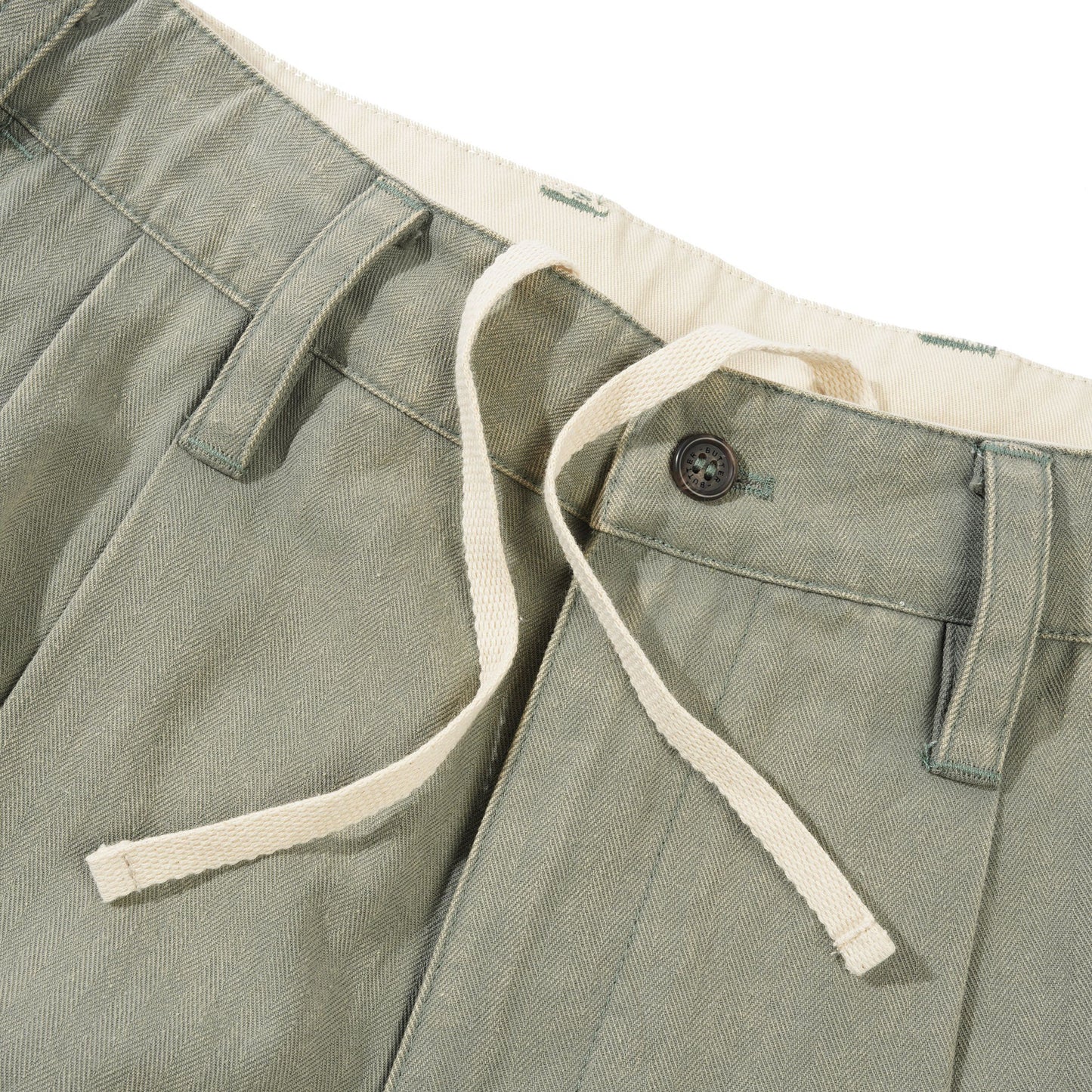 Close-up of green pants with a button and white trim on a white background
