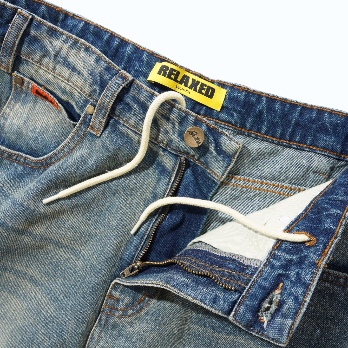 Close-up of a pair of blue denim jeans showing the waistband, white drawstring, zipper pocket detail, and a yellow RELAXED brand label.