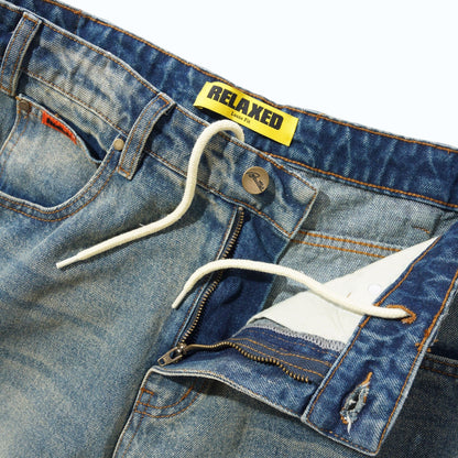 Close-up of a pair of blue denim jeans showing the waistband, white drawstring, zipper pocket detail, and a yellow RELAXED brand label.
