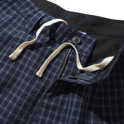 Close-up of a pair of dark blue plaid shorts showing the waistband, beige drawstring, button closure, and zipper detail against a white background.