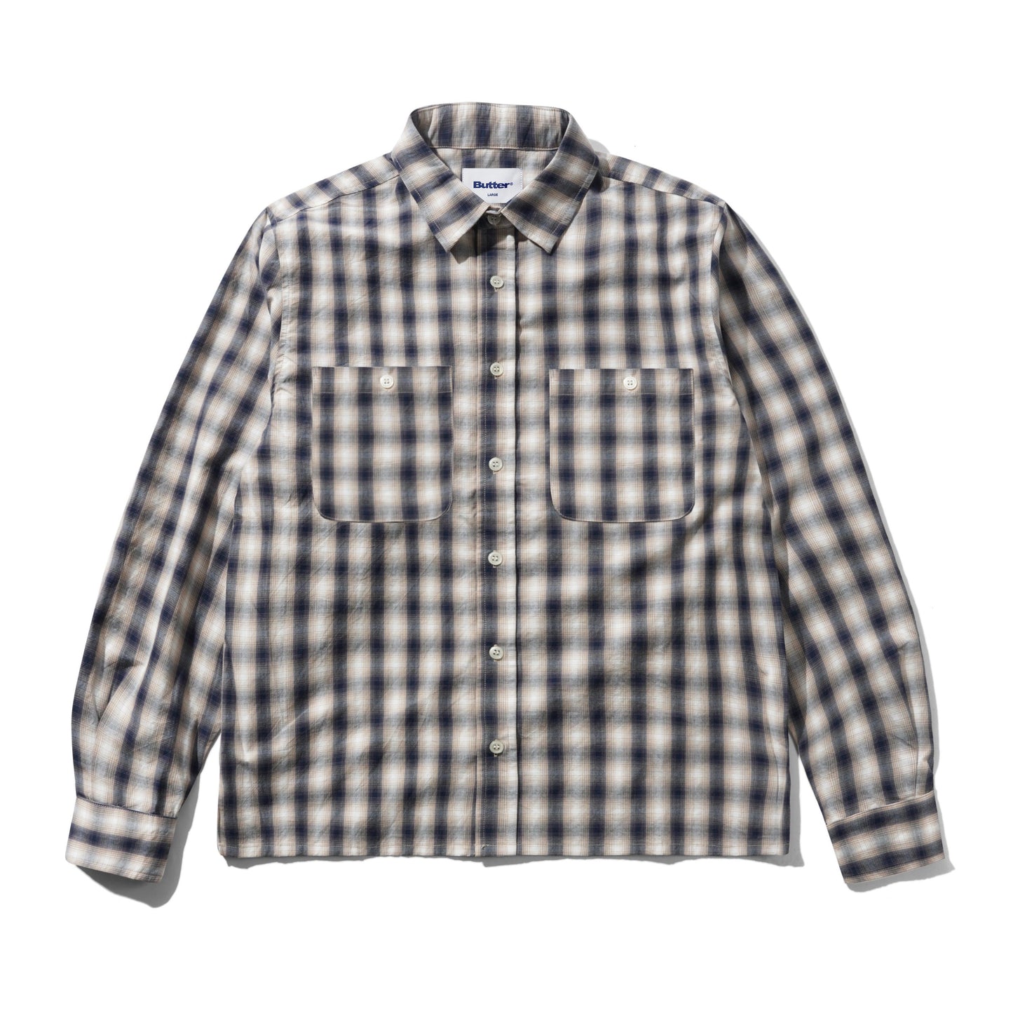 A long-sleeve button-up shirt with a classic plaid pattern in beige, white, and dark navy blue, featuring two buttoned chest pockets and a pointed collar.