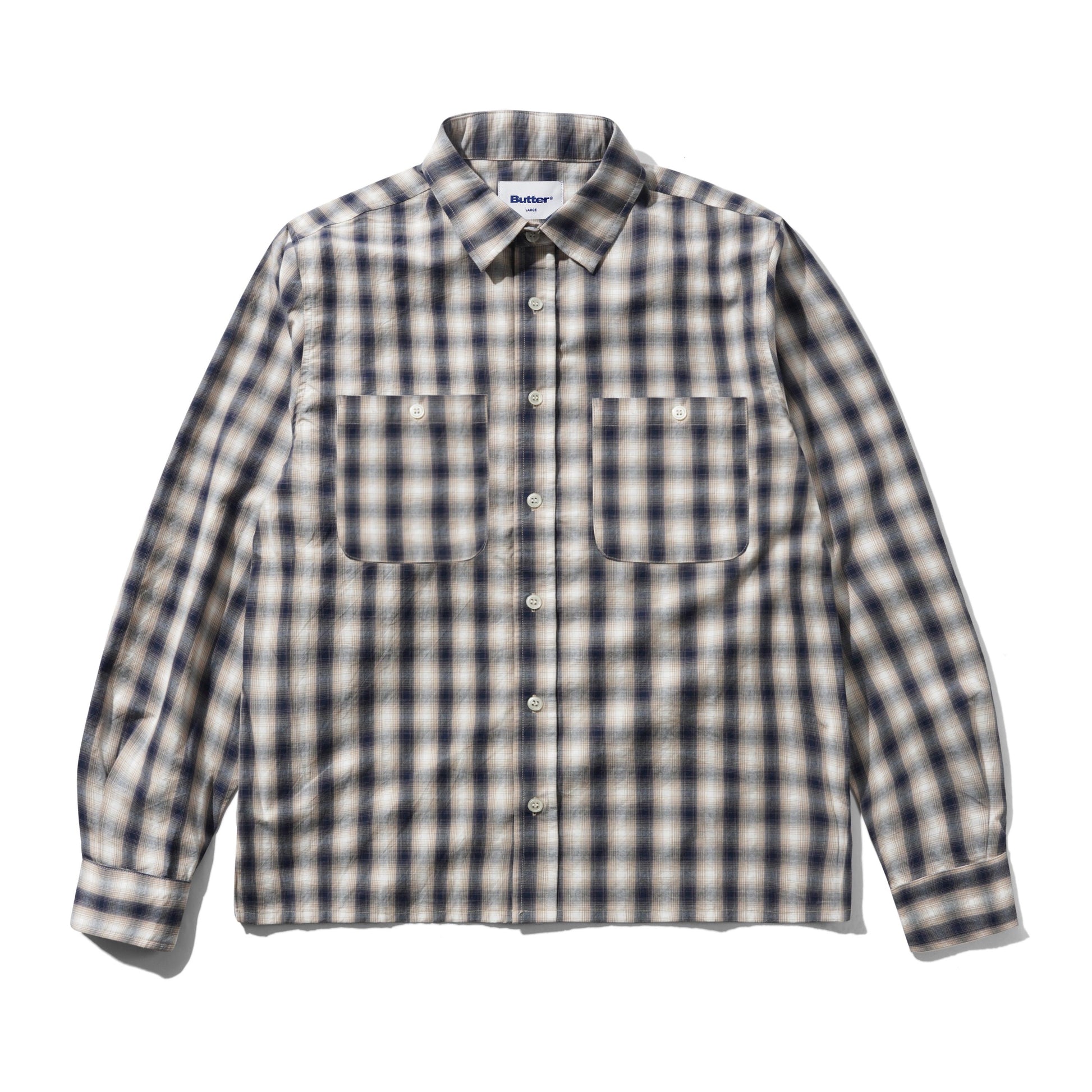 A long-sleeve button-up shirt with a classic plaid pattern in beige, white, and dark navy blue, featuring two buttoned chest pockets and a pointed collar.