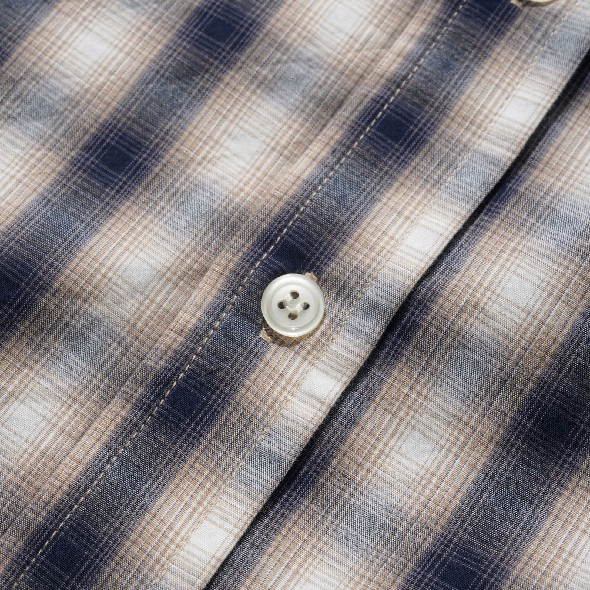 Close-up of a plaid button-up shirt fabric with navy, beige, and white stripes, showing the texture and buttons.