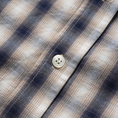 Close-up of a plaid button-up shirt fabric with navy, beige, and white stripes, showing the texture and buttons.