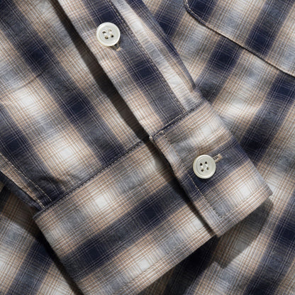 Close-up of a plaid button-up shirt showing the collar, button, cuff, and chest pocket area. The fabric has a navy, beige, and white check pattern.